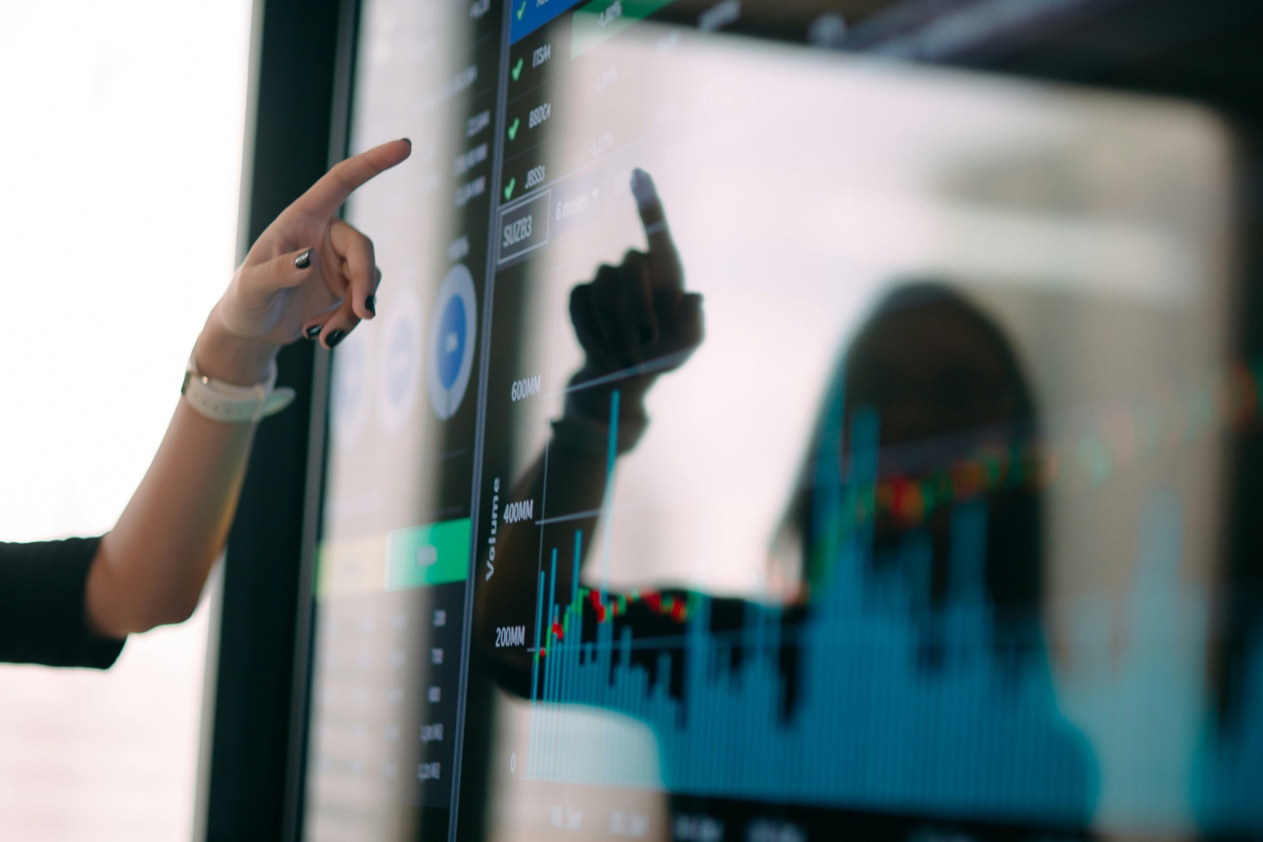 Person pointing at a digital screen displaying financial graphs and data.